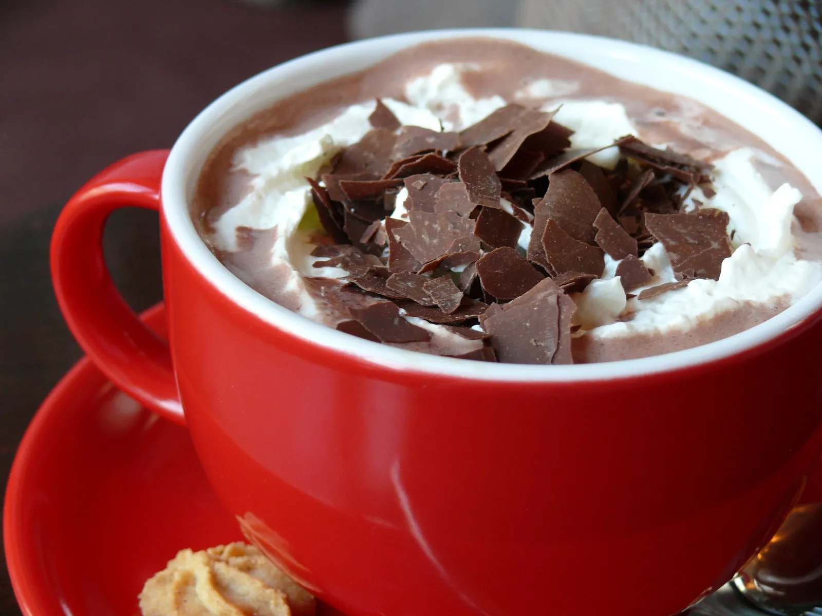 A red mug of hot chocolate topped with whipped cream and chocolate shavings
