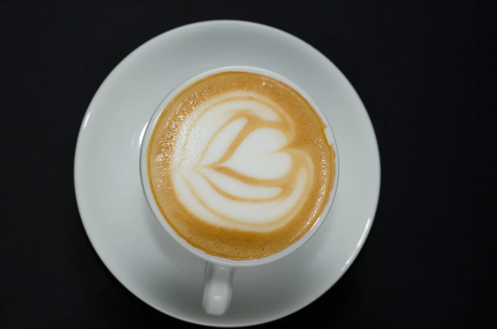 A latte with heart-shaped latte art in a white cup on a saucer